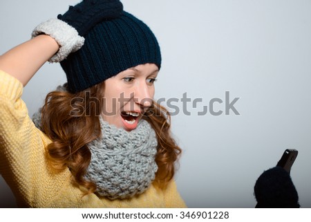 beautiful girl with surprise stares at the phone in a bright yellow color, lifestyle winter clothes studio photo isolated on a gray background