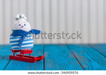 Snowman on a red sled On light wooden background. With empty space for text.