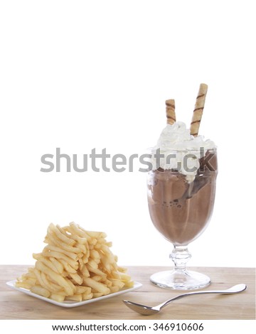Chocolate ice cream in glass cup with whipped cream and square white plate of stacked french fries on a light wood table. Food fad or new trend. Sweet and salty. isolated on white background.