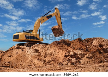 Excavator bulldozer in sandpit with raised bucket over blue cloudscape sky Royalty-Free Stock Photo #34691263