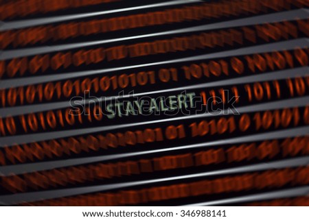 Stay alert text is in the screen. The words are in green and the zeros and ones are in red. Also the text is in focus and the surrounding area is blurred to emphasize the words.
