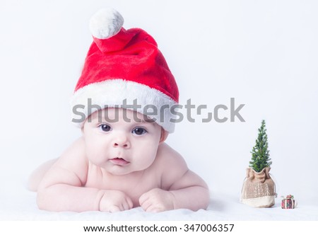 Little Baby Girl with Red Christmas Hat and Tiny Xmas Tree on Clean White Background
