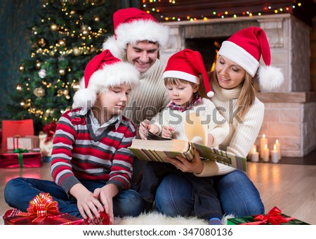 Family reviewing photos in album together near Christmas tree in front of fireplace