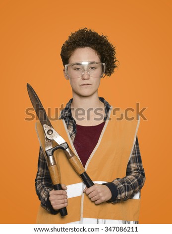 Young woman worker holding pruning shears on orange background