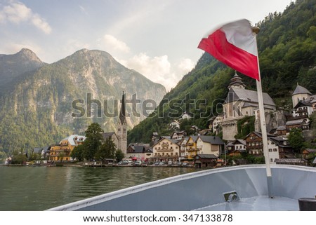 Hallstatt Scenic picture-postcard view of famous mountain village by Lake Hallstatt from Approach Ferry boat with Austrian Flag in the Austrian Alps under Golden Dramatic Sky Sunset in Summer, Austria