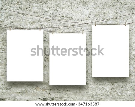 Three empty paper sheet frames hanged by clothes pins on scratched concrete wall background