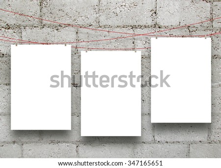 Three empty paper sheet frames hanged by clothes pins on grey concrete blocks background