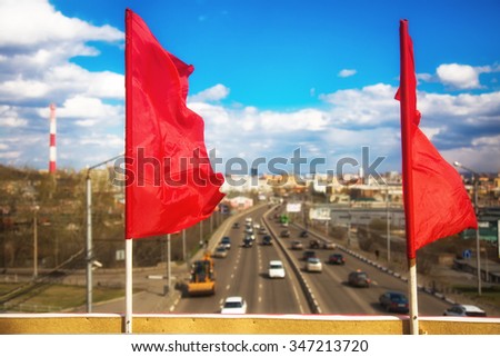 Red flag as a symbol of the holiday on the background of the industrial city with the transport, buildings and roads