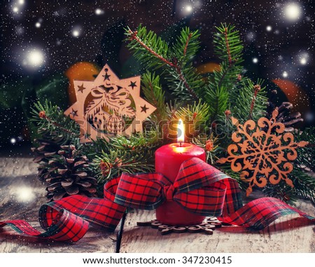 Christmas composition with burning red candles tied with plaid ribbon with a bow, snowflakes, pine cones and spruce branches, dark toned image, selective focus
