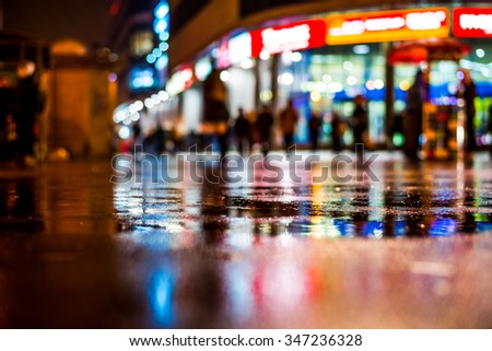 Rainy night in the big city, shop windows glowing in the reflection of asphalt. View from the level of asphalt