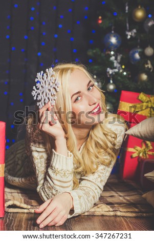 Happy smiling blonde girl with white snowflake are celebrating Xmas near christmas tree at home