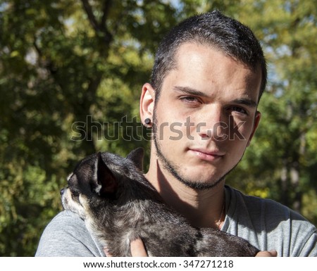 Young man holding cute black chihuahua dog over green nature background