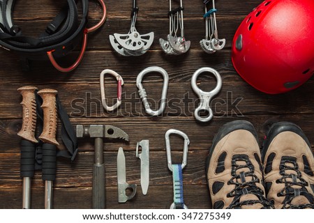 climbing equipment: red helmet, hammer, carabiner, trekking shoes and other set  on dark wooden background, top view Royalty-Free Stock Photo #347275349