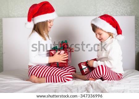 funny kids in their pajamas and Christmas caps on the bed, Christmas and New Year concept, with gifts