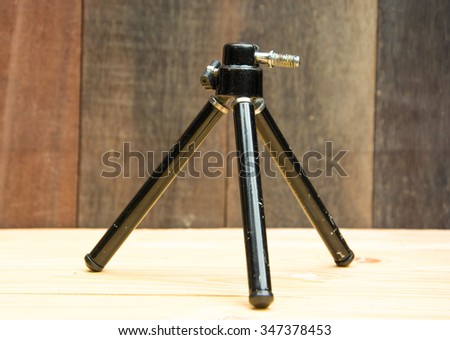 BLACK COLOR-TRIPOD FOR COMPACT CAMERA ON  TABLE , VINTAGE WOODEN WALL BACKGROUND