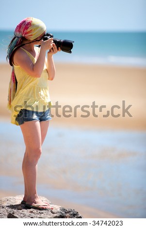 Beautiful young female photographer taking pictures on beach