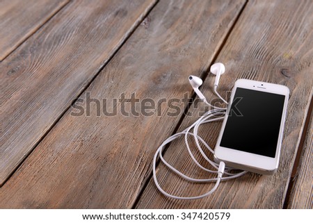 White cellphone with headphones on wooden background