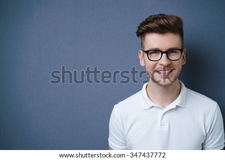 Smiling friendly attractive young man with a modern trendy hairstyle posing against a dark grey background with copyspace, head and shoulders portrait Royalty-Free Stock Photo #347437772