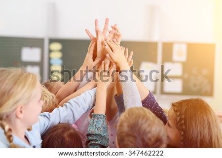Happy Kids Putting their Hands Together in the Air Inside the Classroom. Royalty-Free Stock Photo #347462222