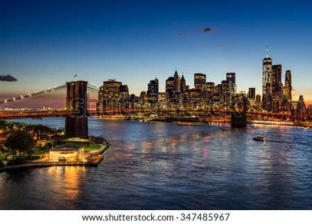 Elevated view of the Brooklyn Bridge and Lower Manhattan skyscrapers at dusk. The illuminated skyline of the Financial District reflects in the East River. New York City.