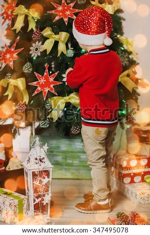 Little child decorating with toys Christmas tree. Vertical color photo