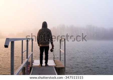 Photographer standing on a pier near a pond in a foggy autumn morning