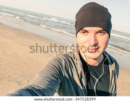 Young handsome guy with male sport clothes taking selfie at beach in autumn season -  Healthy lifestyle and fitness training concept - Vintage desaturated filter look with tilted horizon composition