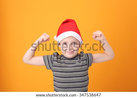 cute little boy wearing Santa Claus cap demonstrating his muscles