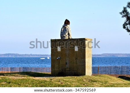 Young boy sitting on a ledge while looking into the ocean
