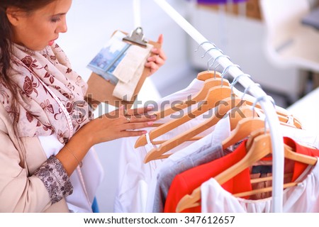 Beautiful young stylist near rack with hangers Royalty-Free Stock Photo #347612657