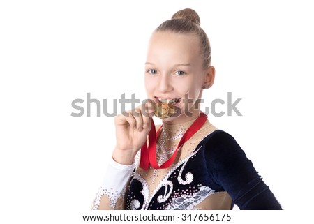 Portrait of beautiful happy smiling cool fit gymnast or skater young woman in sportswear dress posing, jokingly biting golden medal, studio, isolated, white background