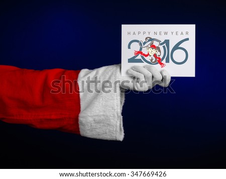 Christmas and New Year 2016 theme: Santa Claus hand holding a white gift card on a dark blue background in studio isolated