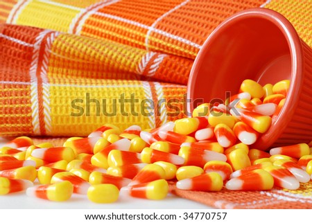 Candy corn spilling from dish with color coordinated fabric in the background.  Macro with shallow dof.