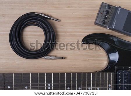 black electric guitar and distortion unit on a wooden background texture