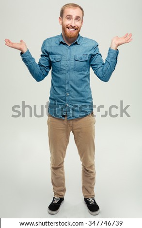 Full length portrait of a smiling casual man shrugging shoulders isolated on a white background