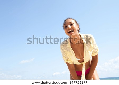 Beautiful african american young woman with perfect skin on a sunny beach against a blue sky and sea, joyfully smiling looking at camera, space. Well being lifestyle, outdoors holiday.