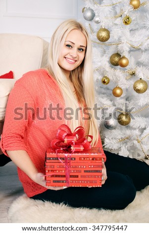 Smiling, long-haired blonde with a Christmas gift in hand, New Year Concept