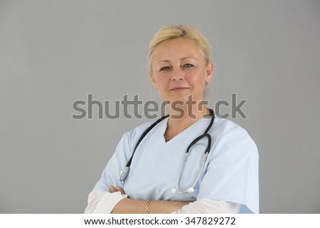Close up of blonde female self confident doctor with crossed arms smiling and looking at the camera
