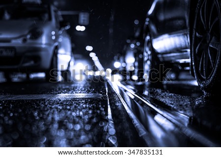 Rainy night in the big city, stream of cars traveling along the avenue. View from the tram rail level, image in the blue toning