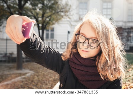 Beautiful Caucasian blond teenage girl taking photo on her smartphone in autumnal park, vintage style tonal correction photo filter