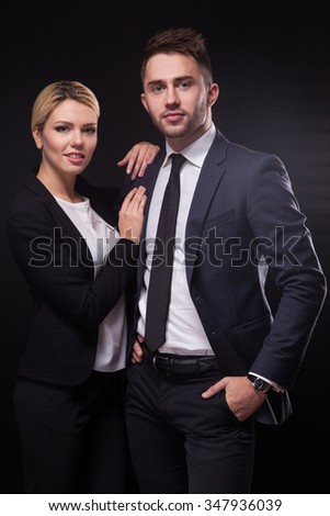 stylish, trendy and modern business man and woman on black background looking confidently at the camera.