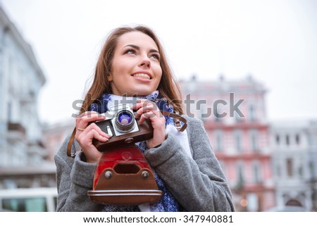 Portrait of a smiling young woman holding retro camera and looking away outdoors