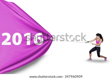 Picture of healthy indian woman wearing sportswear and pulling a big flag with numbers 2016 in studio