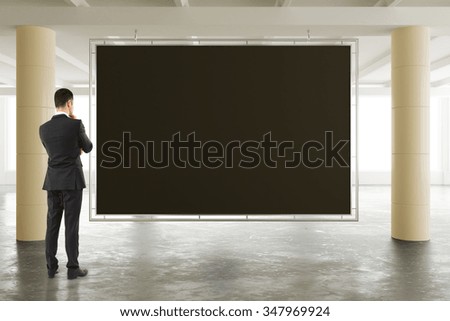 Businessman looking at blank blackboard in sunny spacious hangar area with concrete floor, mock up 3D Render