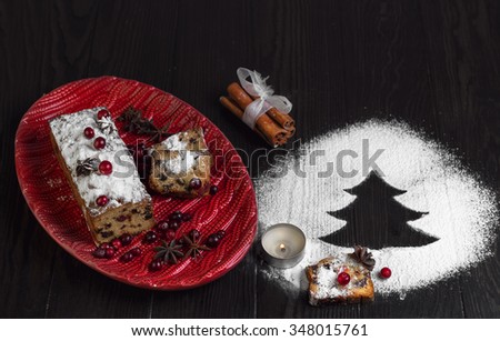 On a wooden desk background Christmas Stollen, Angel, red dish with crochet pattern, powdered sugar like snow, cinnamon sticks, star anise, tree of powdered sugar