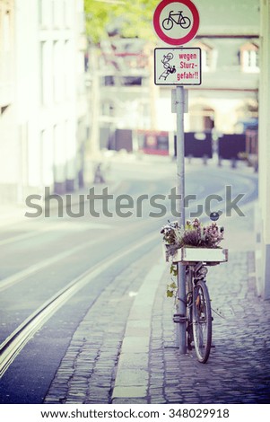 An abandoned bicycle is leaning on a traffic sign in the streets. Some flowers has been planted on wooden box on the bicycle. Image has a vintage effect applied.