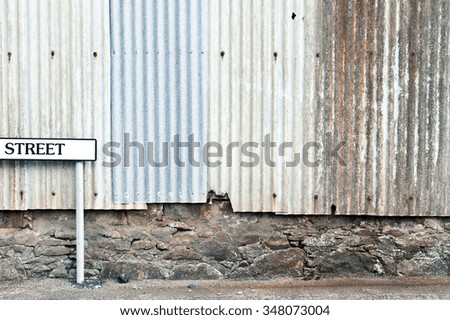 A modern white street sign in front of an old metal building