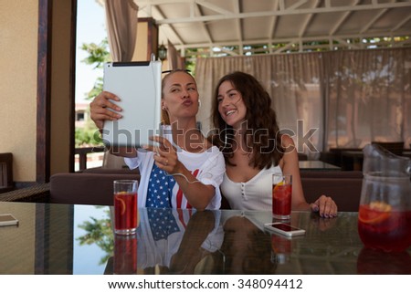 Attractive happy women best friends posing while photographing herself on touch pad for social network picture,cheerful girls making self portrait with digital tablet camera during rest in coffee shop