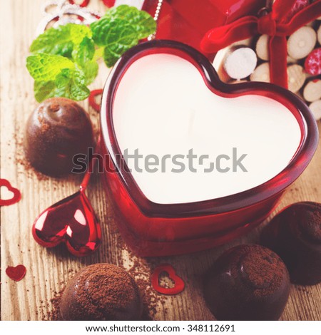 Valentines day composition with chocolate candies, candle and hearts on vintage wooden background. Toned photo.