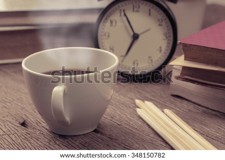 Education concept. Hot coffee with old book and alarm clock on grunge wood table.